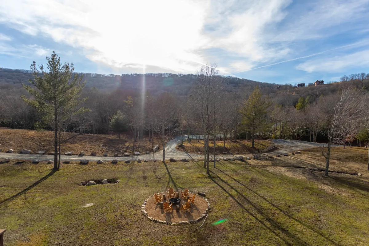 A tranquil outdoor setting featuring a stone fire pit surrounded by wooden chairs, all set against a scenic mountain landscape. The space invites families to gather, toast marshmallows, and share stories under the stars.