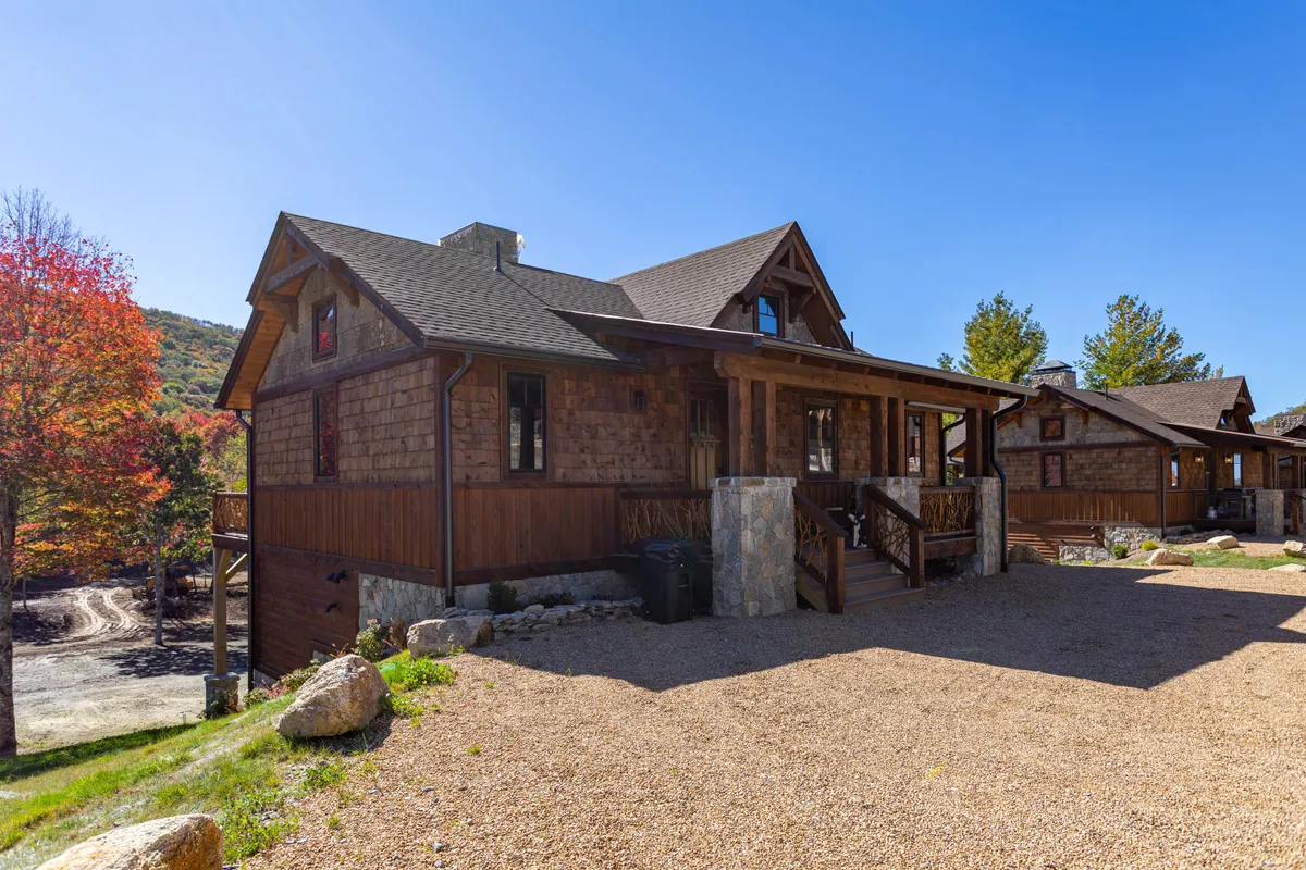 The image showcases the charming wooden exterior of the Three Little Bears cabin, framed by vibrant autumn trees and a spacious gravel driveway. The cozy front porch invites guests to gather and enjoy the natural beauty that surrounds the property.
