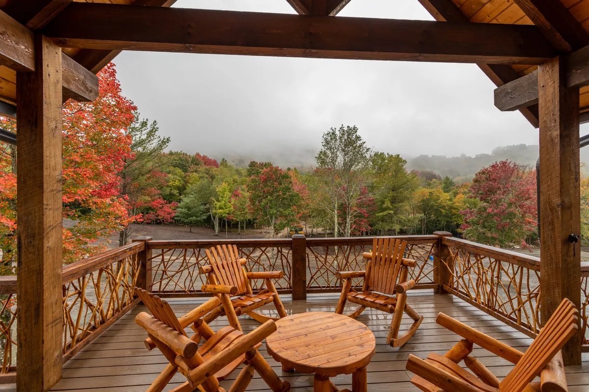 A peaceful wooden deck with rocking chairs and a table, enveloped by surrounding autumn foliage. The view invites relaxation, coffee sipping, and intimate group gatherings while immersed in the sights and sounds of nature.