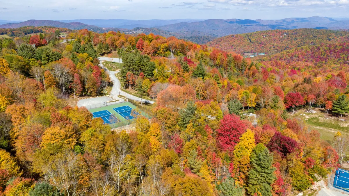 An energetic exterior view of tennis courts nestled among vibrant autumn foliage, with a dramatic mountain range in the distance. The courts are ready for friendly matches, and the surrounding scenery promises refreshing hikes and time in nature.