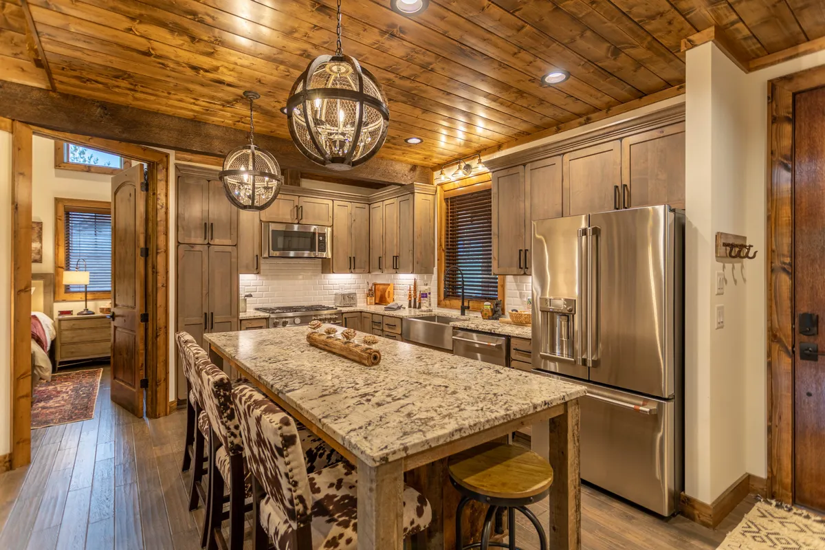 A close-up of the kitchen area with a granite countertop, pendant lighting, wooden cabinetry, and stainless steel appliances, including a modern range. The bar seating at the island is prominent, emphasizing spaces for both cooking and casual dining.