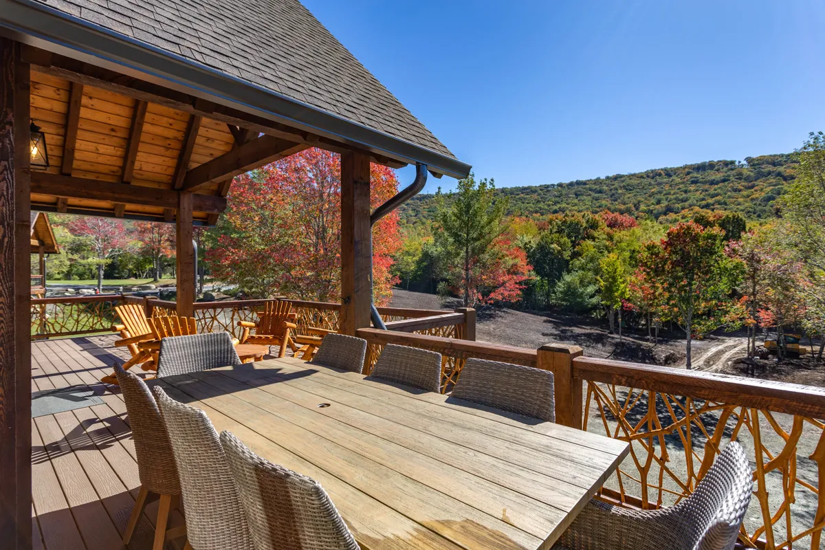 An outdoor wooden dining table surrounded by chairs, set on a patio with vibrant, colorful trees and mountain views in the background. The scene captures the essence of spending time outdoors, enjoying meals or relaxing in nature.